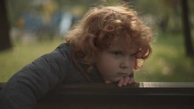 悲伤的男孩坐在公园的长椅上，思念着家人，被遗弃的孩子视频素材