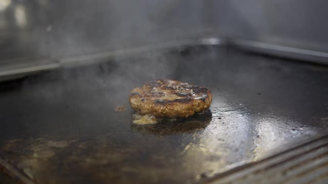 为芝士汉堡烹制牛肉和猪肉馅饼。肉在厨房烤。油滴，烟雾缭绕。视频素材
