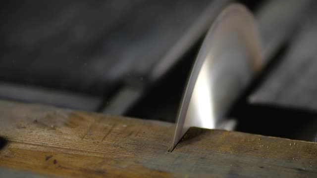 在一个小型家具厂的木工车间里，一个戴着橙色手套的工匠用圆锯将一块木板切成两块，速度为每秒200帧的慢动作。木工、细木工视频下载
