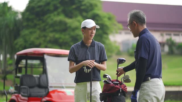 一位亚裔华人父亲在高尔夫球场教儿子打高尔夫球视频素材