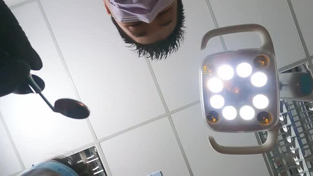 亚洲华裔男牙医，戴着放大镜，用光从上往下看病人视频下载