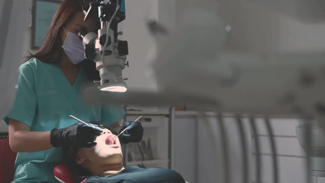 亚洲华裔女牙医在牙医办公室里用显微镜观察病人的牙齿视频素材