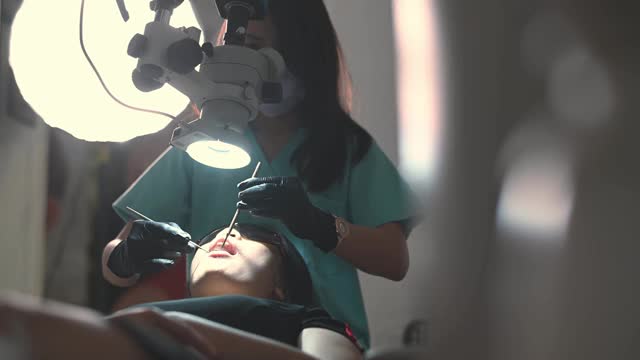 亚洲华裔女牙医在牙医办公室里用显微镜观察病人的牙齿视频下载