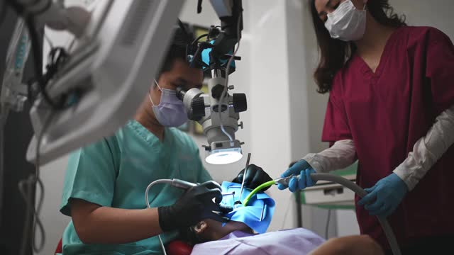 亚洲华裔男牙医在牙科诊所用显微镜观察病人的牙齿视频素材
