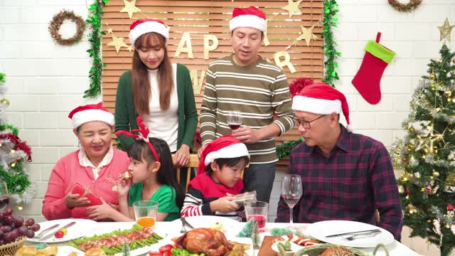 孙辈带着礼物给爷爷奶奶一个惊喜，东南亚几代同堂的家庭团聚，围坐在可爱的餐桌上一起吃圣诞大餐，庆祝12月的节日，用树木装饰家里，装饰装饰。视频素材