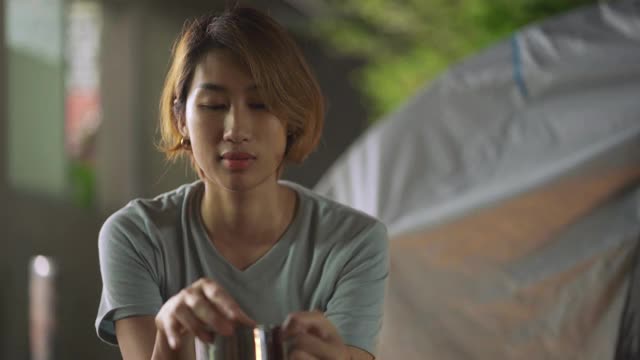 亚洲华人妇女从水壶里倒热的青色水，在他们家的后院的帐篷露营前喝，在家度假的周末活动视频下载