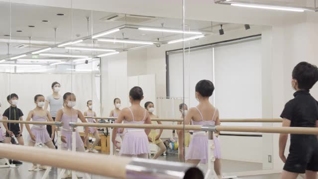 亚洲儿童芭蕾舞学生和镜子里的亚洲教练正在芭蕾舞课吧的工作室里上课。视频素材