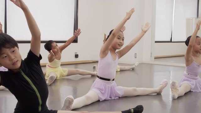 一个芭蕾舞学生的亚洲女孩坐在工作室的地板上做伸展运动。视频素材