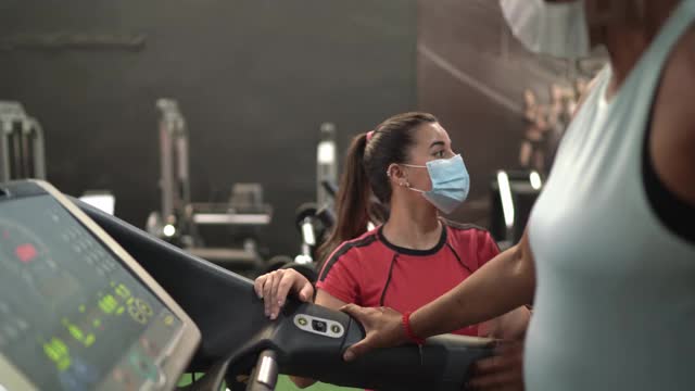 年长的妇女在教练的帮助下在健身房使用跑步机-使用面罩视频下载