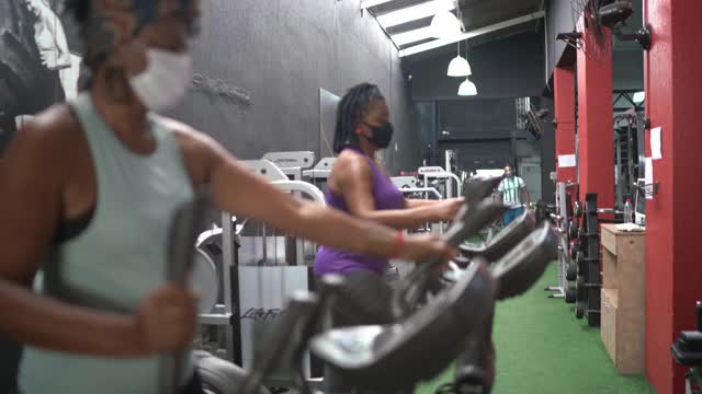 资深同事在健身房锻炼，由私人教练指导，佩戴口罩视频下载