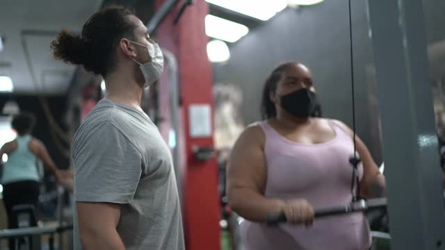 私人教练帮助年轻女子在健身房使用面罩做运动视频素材