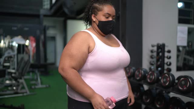 年轻女子在健身房戴着口罩举重视频素材