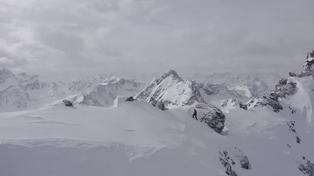 在奥地利阿尔卑斯山脉，一名登山者正走在冰雪覆盖的山脊上，雪花吹在他的脸上视频素材