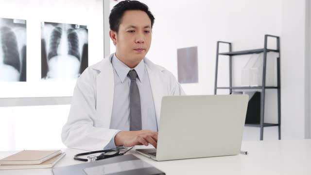 严肃的亚洲男医生正在用剪贴板与女病人坐在医院办公室的桌子前，传递好消息，谈论结果或症状。视频素材