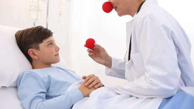 医生儿科医生小丑红鼻子和快乐的儿童病人躺在医院的床上，用替代疗法来振奋孤独视频素材