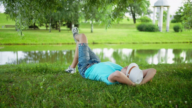 一个戴着白帽的男人正躺在城市公园的草地上休息视频下载