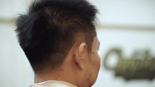一名男子在理发店里拜访发型师，理发师正在给他理发，理发师用剪刀和梳子视频下载