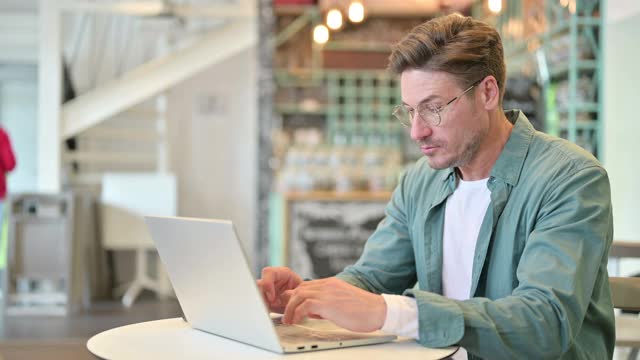 压力中年男子与笔记本电脑在咖啡馆头痛视频素材