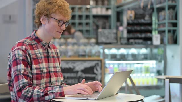 年轻的红发男子用笔记本电脑显示拇指向下视频素材