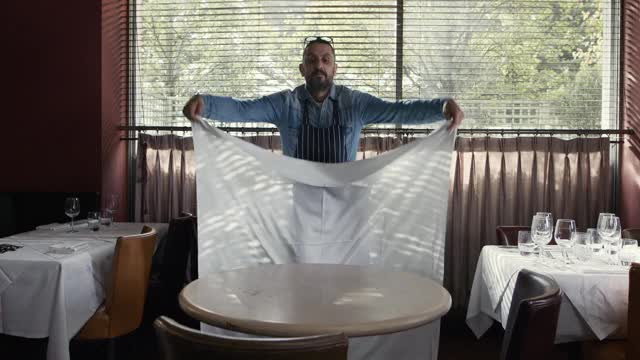 在餐馆里，一个男人把桌布铺在桌子上视频素材