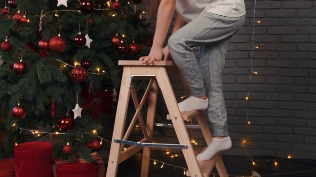 戴着圣诞帽的女孩爬上梯子去摸圣诞树视频下载
