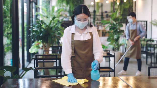 两位年轻的亚洲女服务员戴着防护手套和面罩为桌子消毒视频素材