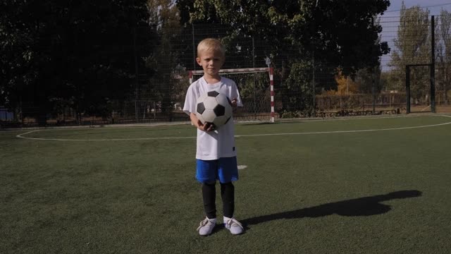 一个小男孩足球运动员在足球场上训练，他在装球。视频素材