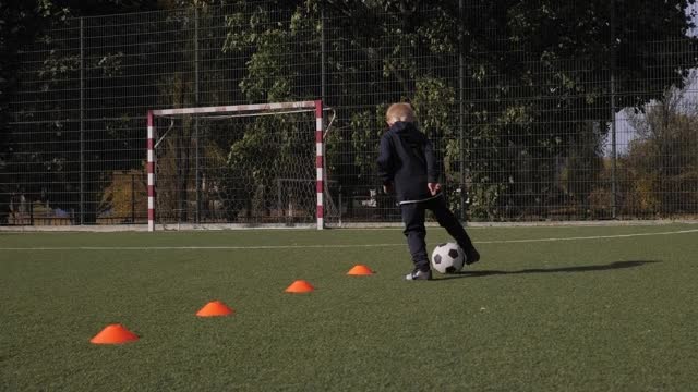 一个小男孩在橙色的圆锥体之间训练运球。足球足球训练。视频素材