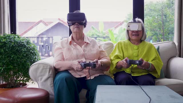 亚洲资深女性朋友喜欢戴着虚拟现实眼镜一起在家客厅玩电子游戏视频下载
