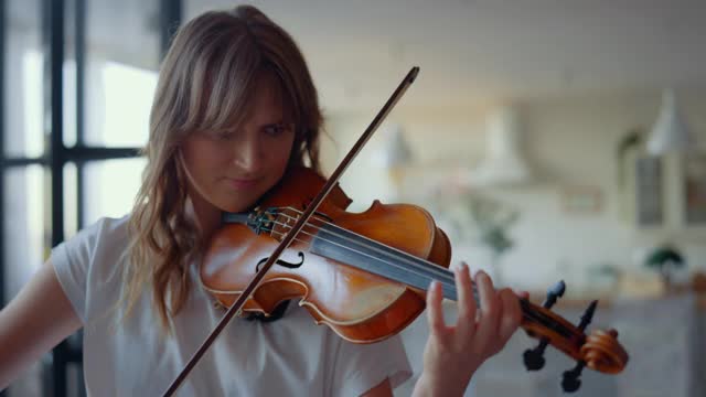 在房间里拉小提琴的女人。少女用弦乐器创作音乐视频下载