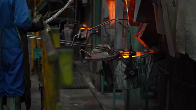 在铸造厂，操作人员将熔化的金属从熔炉中挤出，然后浇注到钢包中视频素材