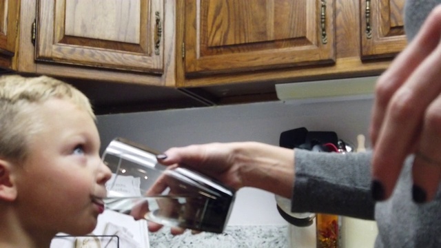 在家庭厨房4K慢动作视频系列中，千禧一代的母亲和两个儿子在用玻璃杯过滤饮用水视频素材