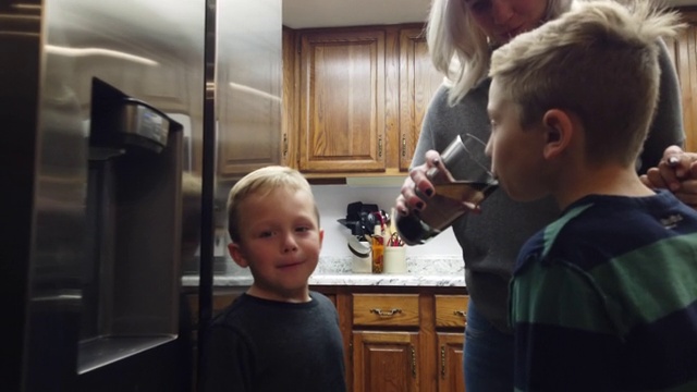 在家庭厨房4K系列视频中，千禧一代的母亲和两个儿子在用玻璃杯过滤饮用水视频素材