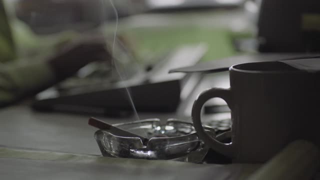一个男人喝咖啡和抽烟在办公室工作的特写镜头视频下载