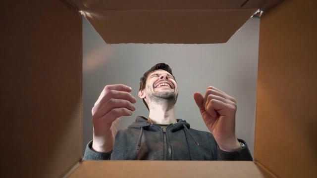 年轻快乐的男人正在打开礼物，看里面的纸箱。视频素材