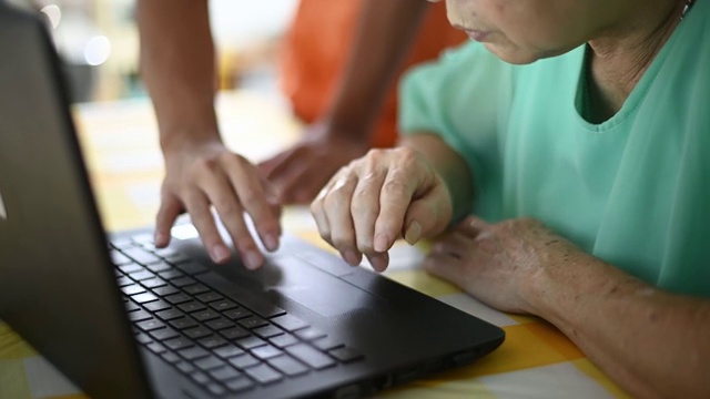 在餐厅里，一位年长的亚洲华人女士向她的孙子学习如何使用笔记本电脑社交媒体视频下载