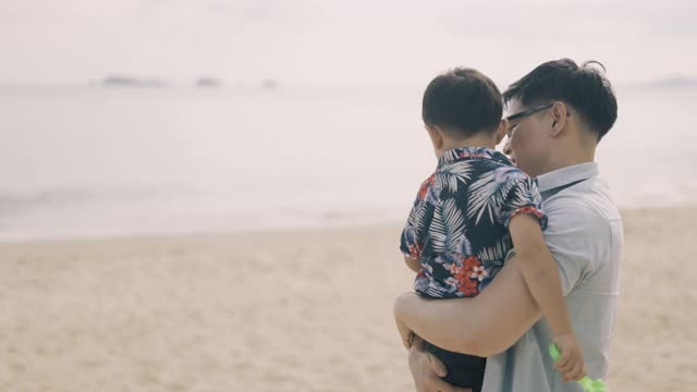 亚裔父亲抱着儿子在海滩上散步视频素材
