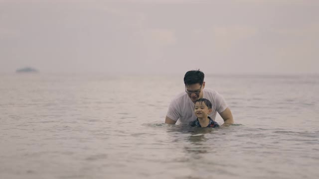 在海滩上，父亲把儿子从海水中抬起来视频素材