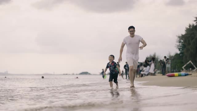 一个亚洲男人在海滩上追着儿子跑视频素材