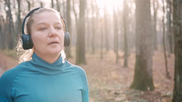 SLO MO女子摘下耳机，走在秋天的森林里视频素材