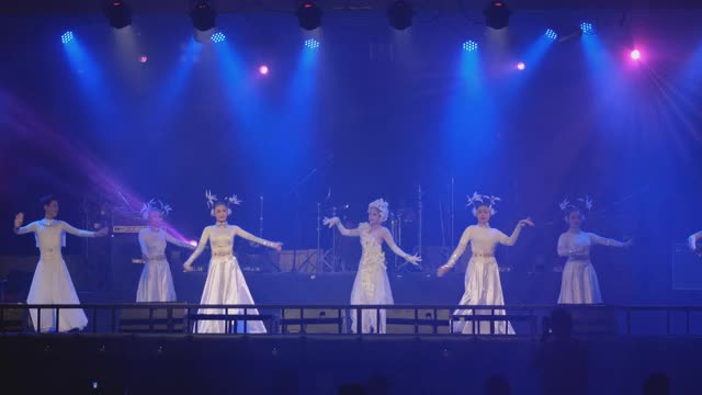 一组亚洲舞者与白色和闪亮的服装展示在舞台上与不同颜色的迪斯科灯视频下载