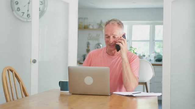 退休老人在家厨房用笔记本电脑打电话庆祝好消息或胜利视频素材