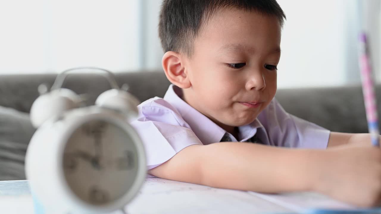 亚洲男孩做家庭作业的意图。一个男孩拿着铅笔写，一个男孩在白纸上画在桌子上，小学和家庭教育，远程在线教育概念。视频下载