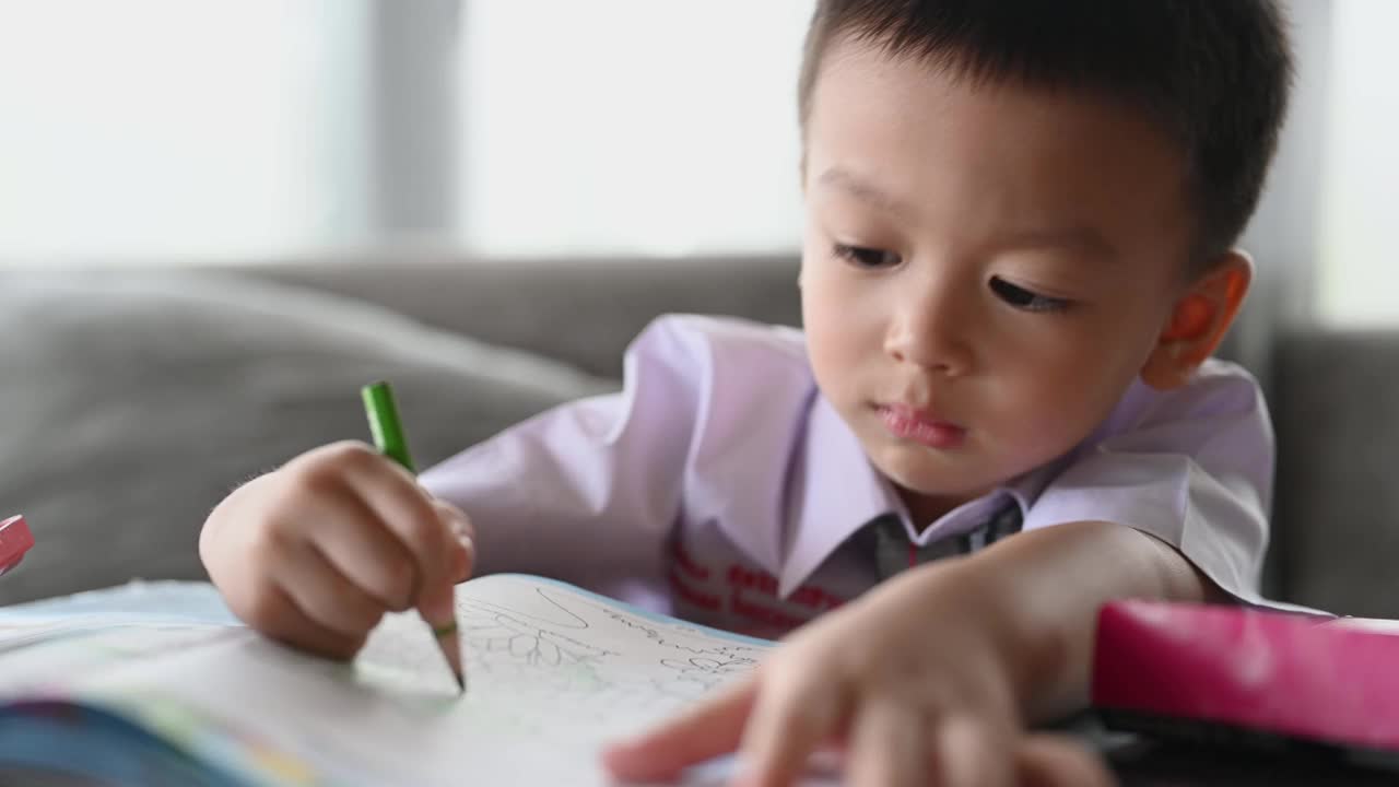 亚洲男孩做家庭作业的意图。一个男孩拿着铅笔写，一个男孩在白纸上画在桌子上，小学和家庭教育，远程在线教育概念。视频下载