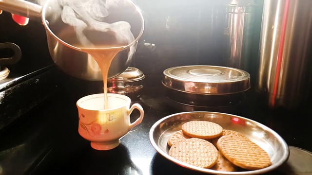 慢动作4K视频热茶(混合牛奶)/咖啡从水壶倒入杯子在早晨的阳光下在厨房和饼干盘视频下载