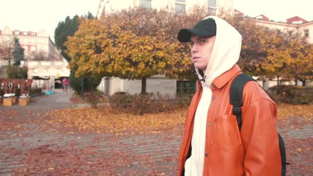 一个戴着兜帽的年轻人在秋天的城市里走来走去。视频素材