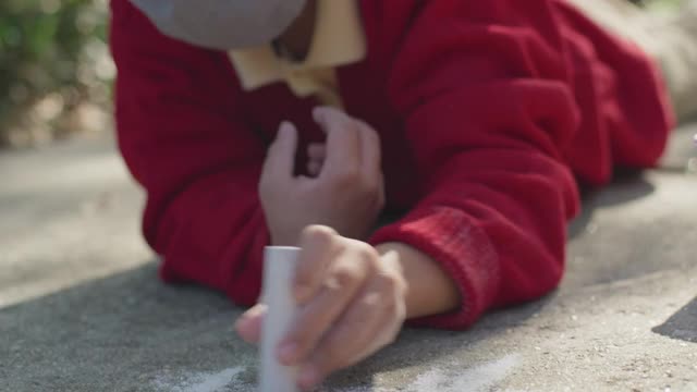 SLO MO CU创意小男孩戴着面具，用彩色粉笔在人行道上画画视频素材