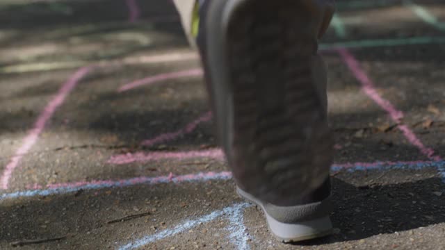 顽皮的小男孩跳下粉笔画的跳房子在人行道上视频素材