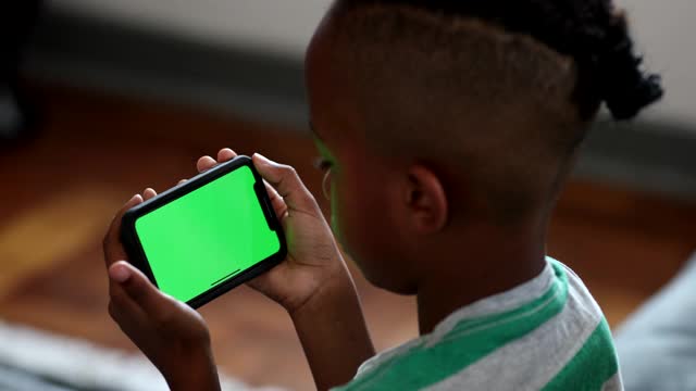 非洲儿童持有智能手机与彩色绿色屏幕模拟。孩子看着空白的屏幕视频素材