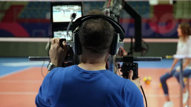 一名摄影师在一个电视节目中使用相机三角架，节目中有一名年轻的男女主持人。体育新闻。视频素材